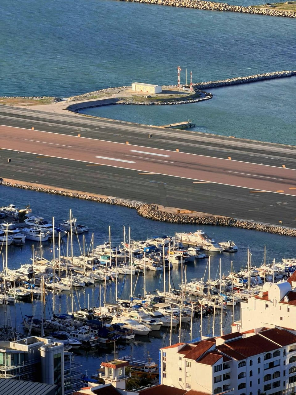 Boats moored in a marina beside the airport runway, seen from above