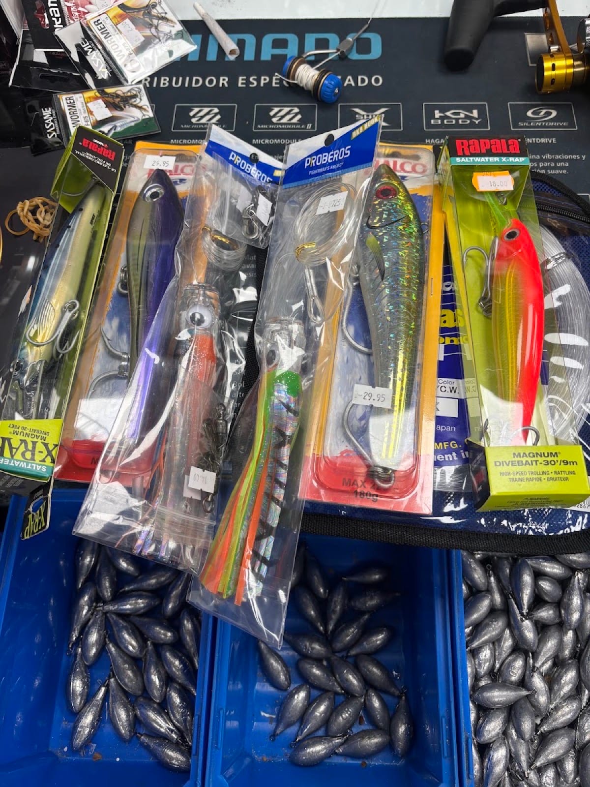 Lure packs pinned to the navy Shimano dealer mat above blue trays of lead sinkers
